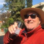 a man wearing a hat and sunglasses holding a glass of ouzo