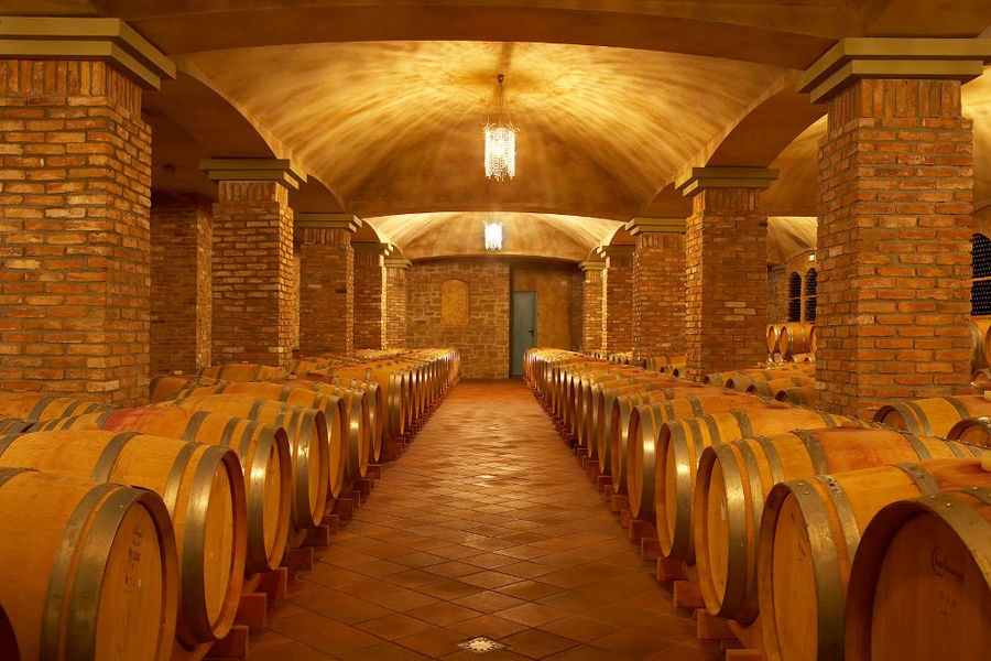 lying wooden barrels in a row at illuminated 'Wine Art Estate' cellar with stone columns