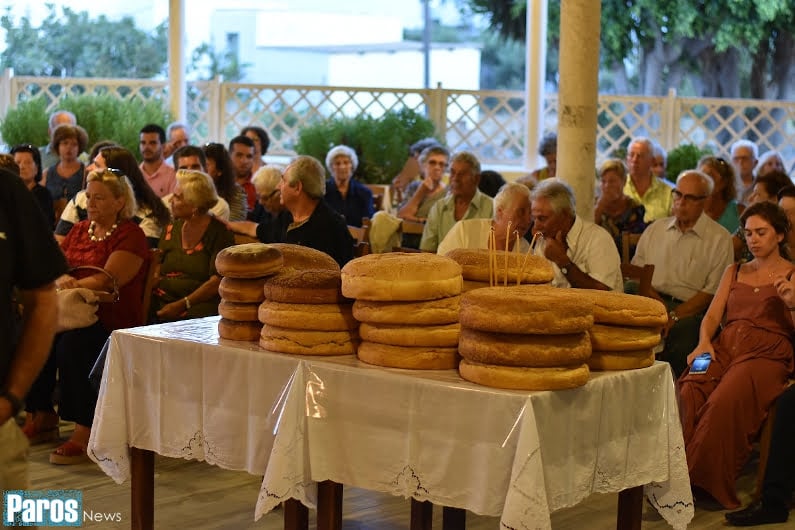 Spherical breads on the table and people sitting outside at church of St. Fanourios, in Paros, Ampelas, that commemorate festival of her birth 