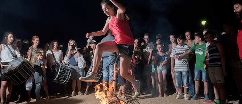 girl jumps fire at Festival of St. John the Baptist, Paros, surrounded by peoples with camera