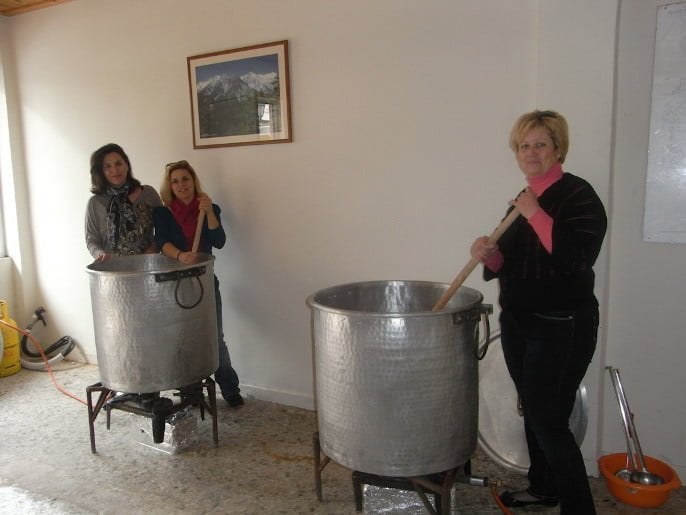 women mixing with wooden rod in a bronze cauldron and watching at the camera at the Festival of Bean Soup at Thebes, Greece