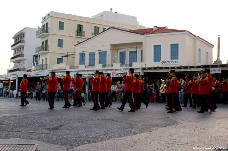marching band with red uniforms walking at ‘The Rite of Love’ at Tinos, Ktikados on street
