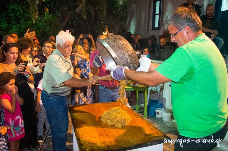 two men overturning was with ‘pasteli’ composition on the table at the Pasteli Festival, Amorgos, Chora, Greece surrounded by people by night 