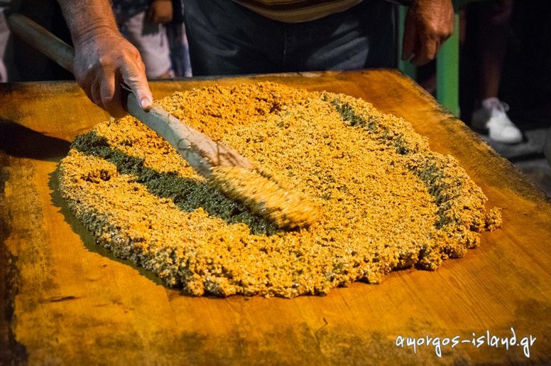 man lying  ‘pasteli’ composition on the table with a wooden spoon at the Pasteli Festival, Amorgos, Chora, Greece surrounded by people by night 