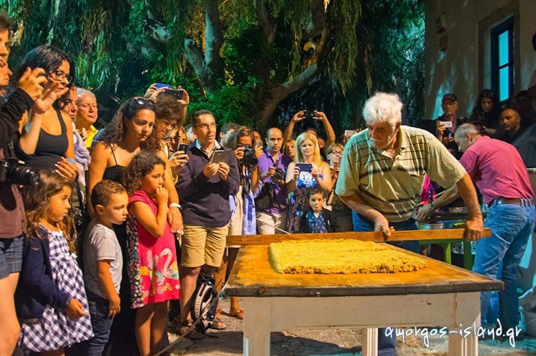 man lying  ‘pasteli’ composition on the table with a wooden spoon at the Pasteli Festival, Amorgos, Chora, Greece surrounded by people by night 