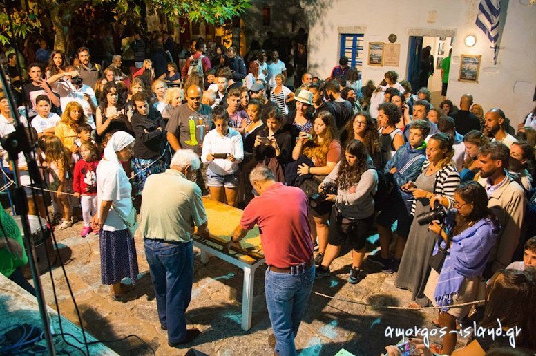 man lying ‘pasteli’ composition on the table at the Pasteli Festival, Amorgos, Chora, Greece surrounded by people by night 