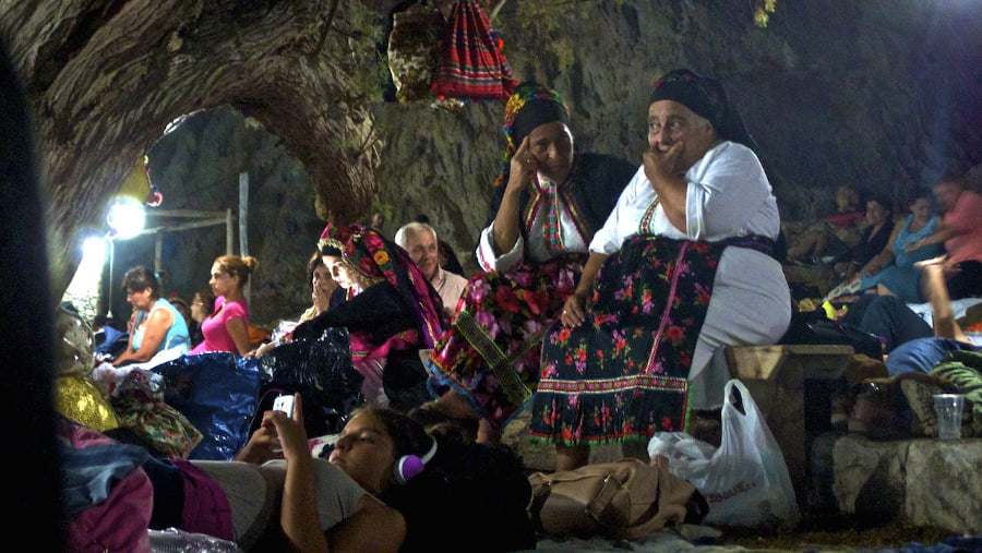 women dressed with folklore cloths sitting at monastery of Ai Giannis area, in Lakki, Greece by night and commemorate festival of her birth