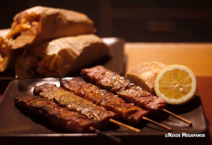 close-up of wooden sticks with cooked Greek souvlaki on plate and a half of lemon|