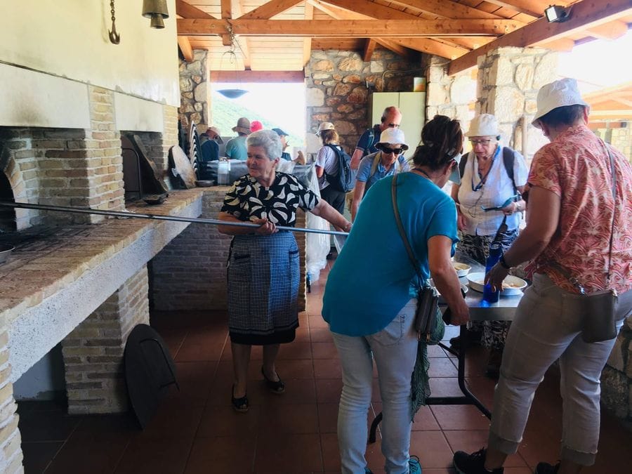 Α lady puts bread in the wood oven and the visitors prepare the bread