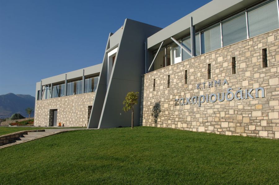 the stone building says on the wall 'KTHMA ZAXARIOYDAKH'and the entrance has lawn green and steps on both sides