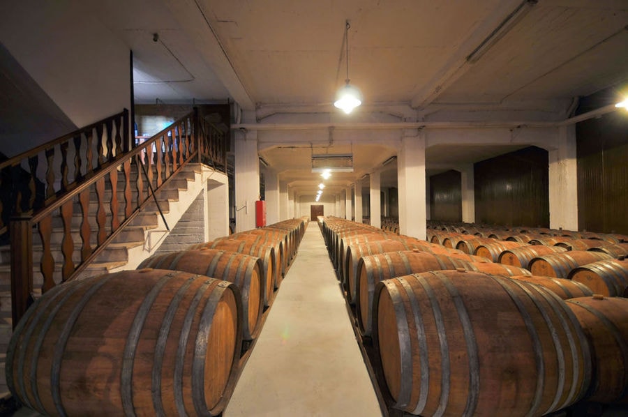 lying wine barrels in a row and a wood staircase at illuminated 'Vaeni Naoussa' cellar