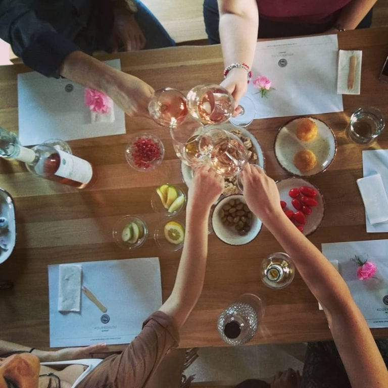 four tourists clink glasses for 'cheers' and eating aperitifs at 'Kourkoulou Winery'