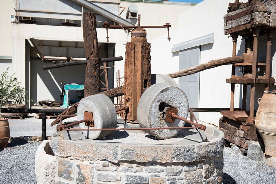 stone old olive press outside at 'Vassilakis Estate' with walls of the building in the background