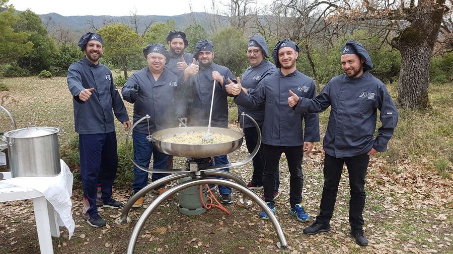 chefs cooking pasta in a large pot in nature around the area of 'Mushroom Museum Meteora'