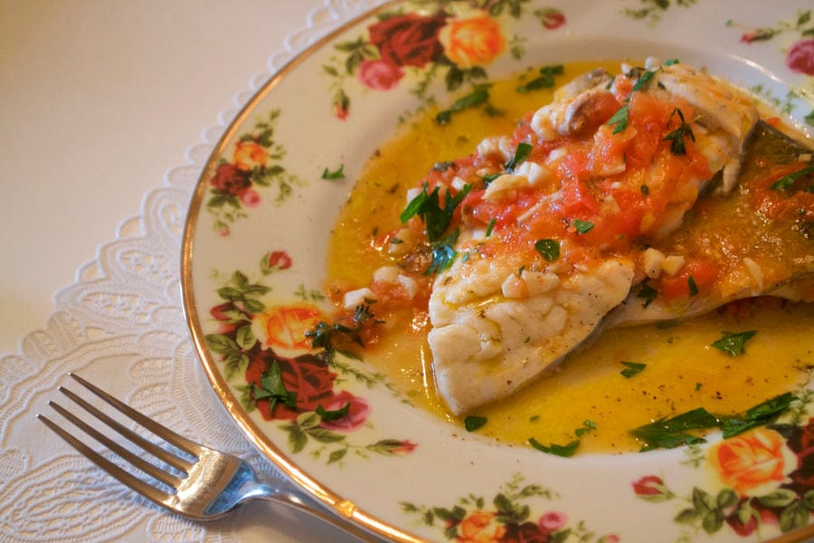 Fillet of fish with tomatoes sauce on plate with flowers at En Kefallinia Organic Farm Restaurant