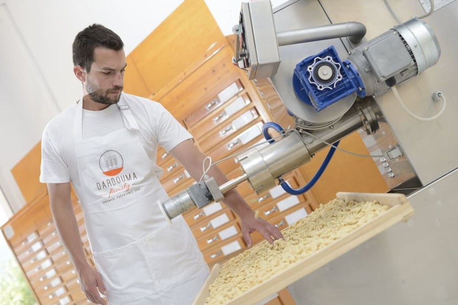 man dressed with t shirt that says 'DARDOUMA family' working pasta production machine