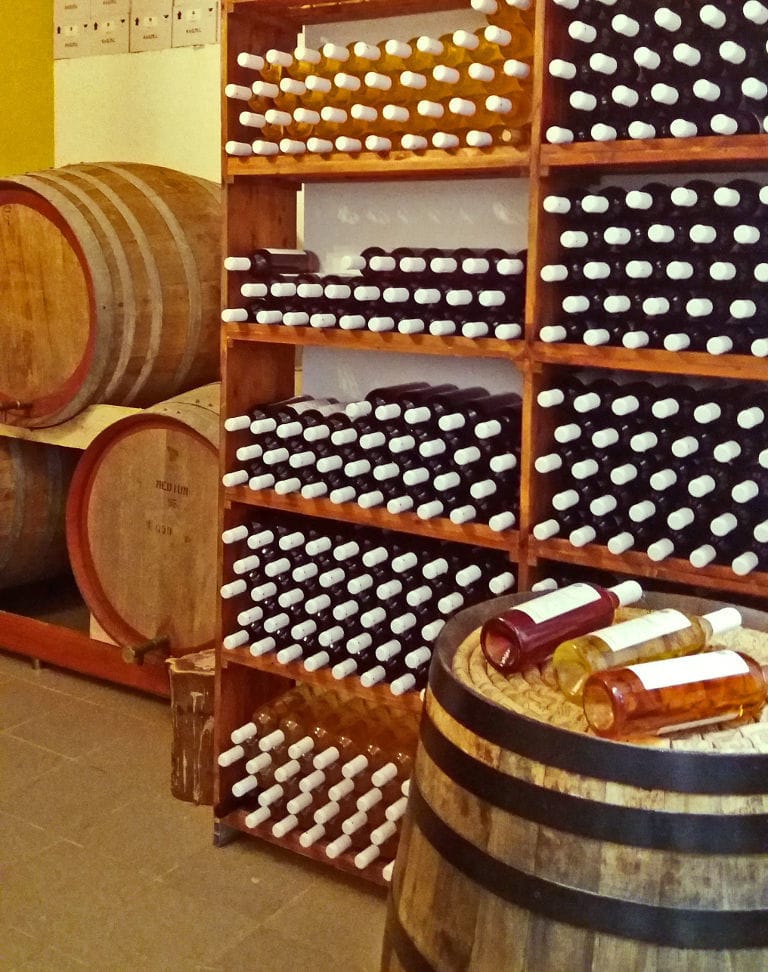 wood barrels and wine bottles on top of each other in the storage lockers at 'Kourkoulou Winery' cellar