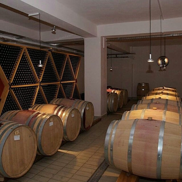 bottles in the storage lockers and lying wooden barrels in a row at 'Zoinos Winery' cellar