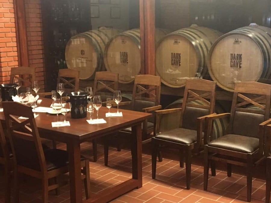 'Tsililis' tasting room with wood table and chairs and glasses and four barrels on the wall