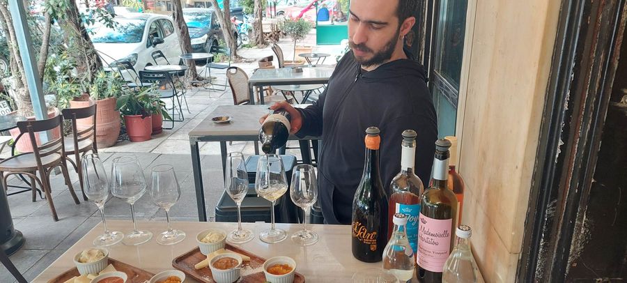 A man pours wine into glasses, with an assortment of delicacies in front of him.