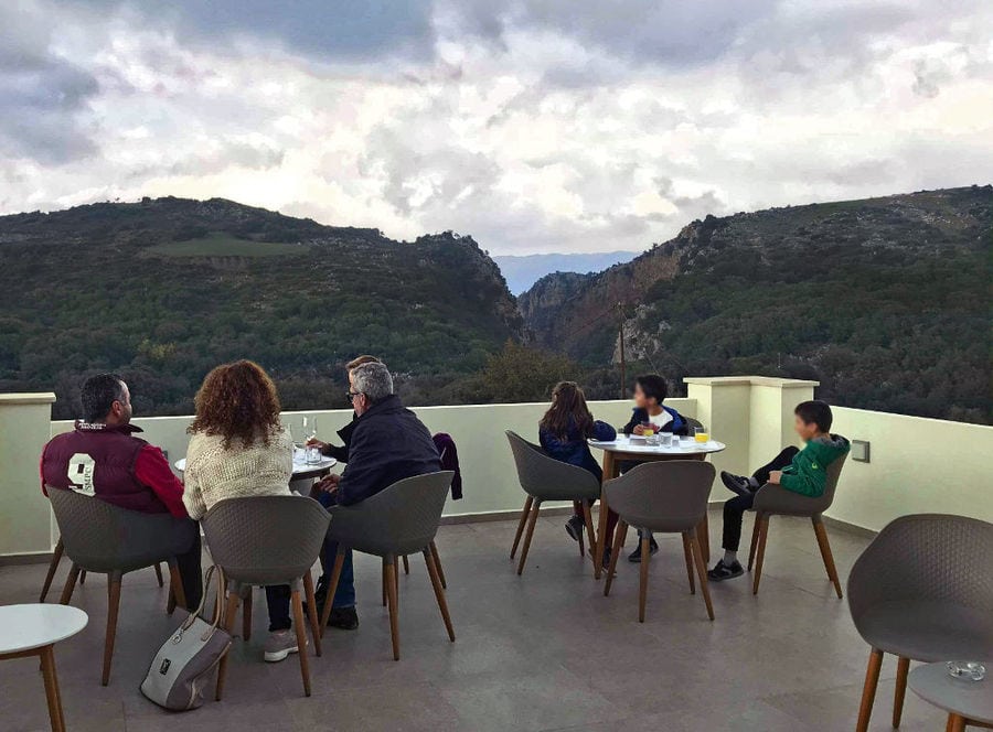 tourists sitting at the tables and admiring the mountains at 'Kourkoulou Winery' terrace