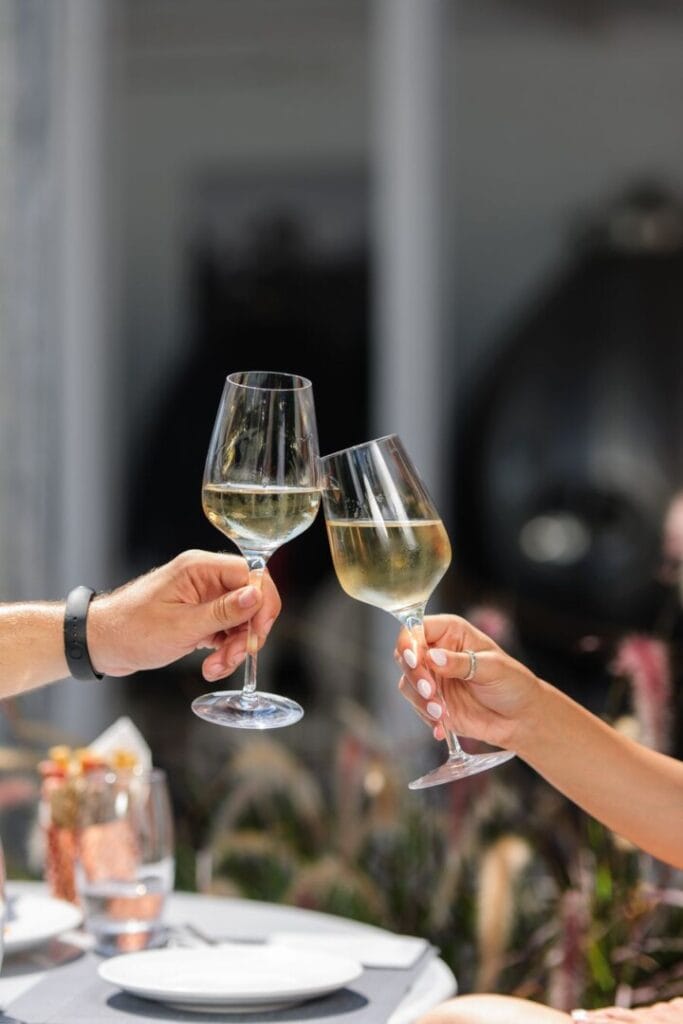 Two hands holding elegant glasses of white wine, coming together in a joyful clink. A celebration of shared moments and the pure delight of raising a toast in unison.