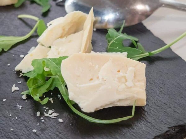 Close-up of slices of Arseniko Naxos cheese and fresh herbs on wooden surface