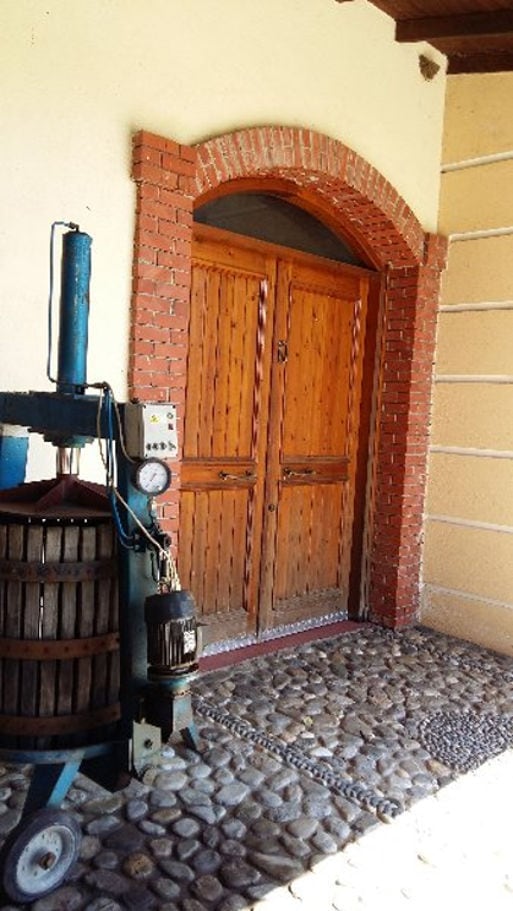 'Foundi Estate' entrance with stone arcade and wood duble door and old press grapes on the one side