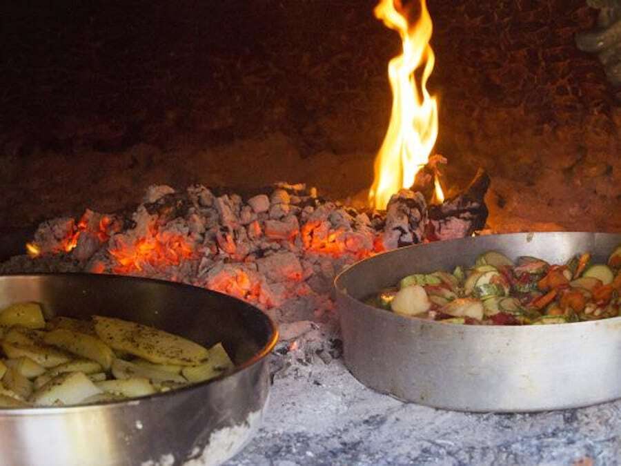 pans with various food represent Gastronomy of Peloponnese with a fire in the background