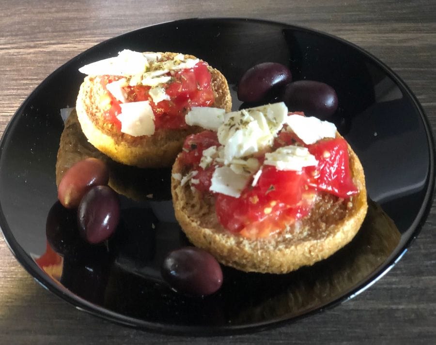 A captivating image reveals a black plate adorned with paximadi, tomatoes, and feta cheese, topped with a drizzle of exquisite olive oils.