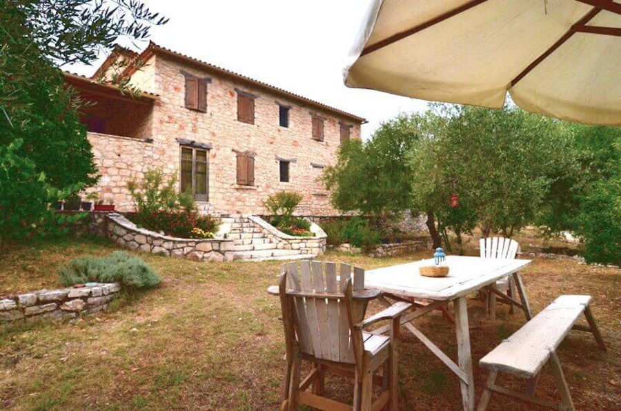 wood table with chairs and a benche in the shade of the umbrella into Goumas Estate garden