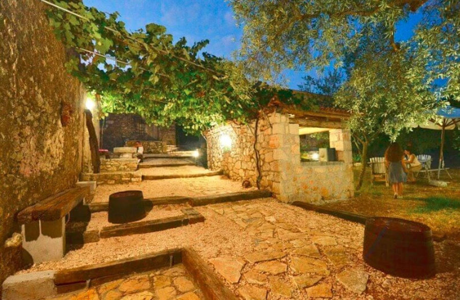 Goumas Estate stone alley with benches and tourists in the garden by night