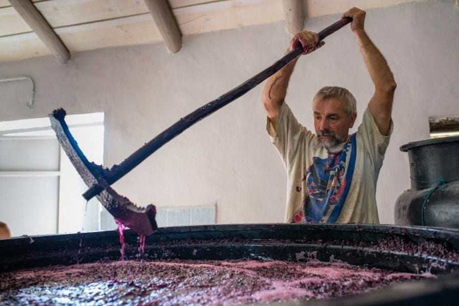 man mixing with a long tool in a cauldron, mass of the must pulp of black grapes at Goumas Estate facilities