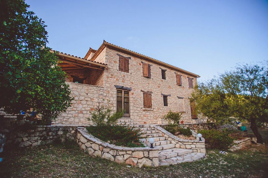 on side of Goumas Estate stone building with wood windows surrounded by green grass and trees