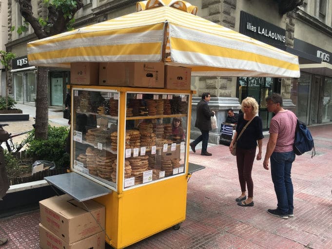 Kiosk with Greek ‘Koulouri’, round-shaped breads topped with sesame seeds on the street and a couple watching them 