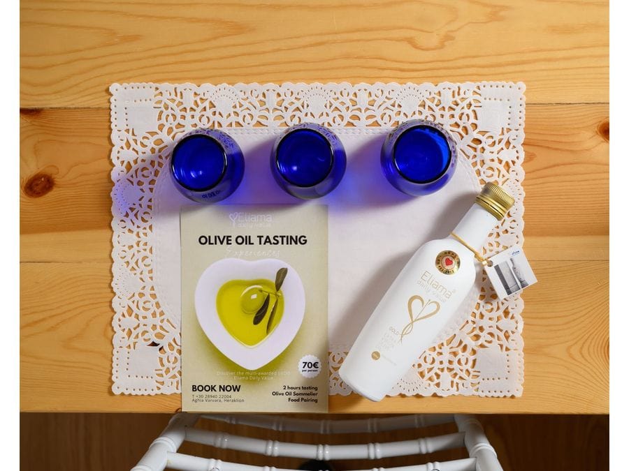 A white place mat hosts three empty blue glasses. On the left, an olive oil tasting book rests beside them. To the right, an olive oil bottle awaits, setting the stage for an enlightening tasting experience.