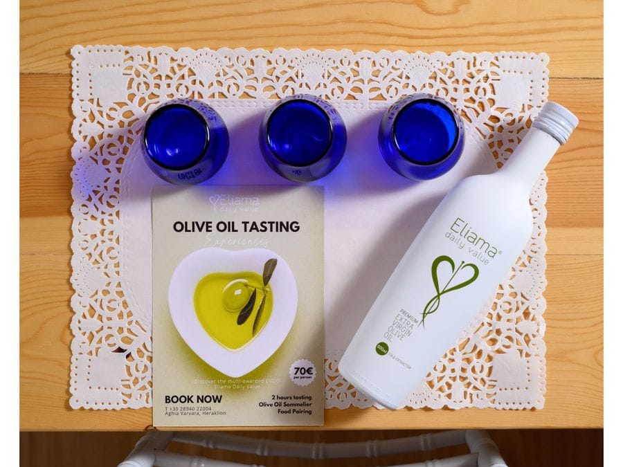 A white place mat hosts three empty blue glasses. On the left, an olive oil tasting book rests beside them. To the right, an olive oil bottle awaits, setting the stage for an enlightening tasting experience.