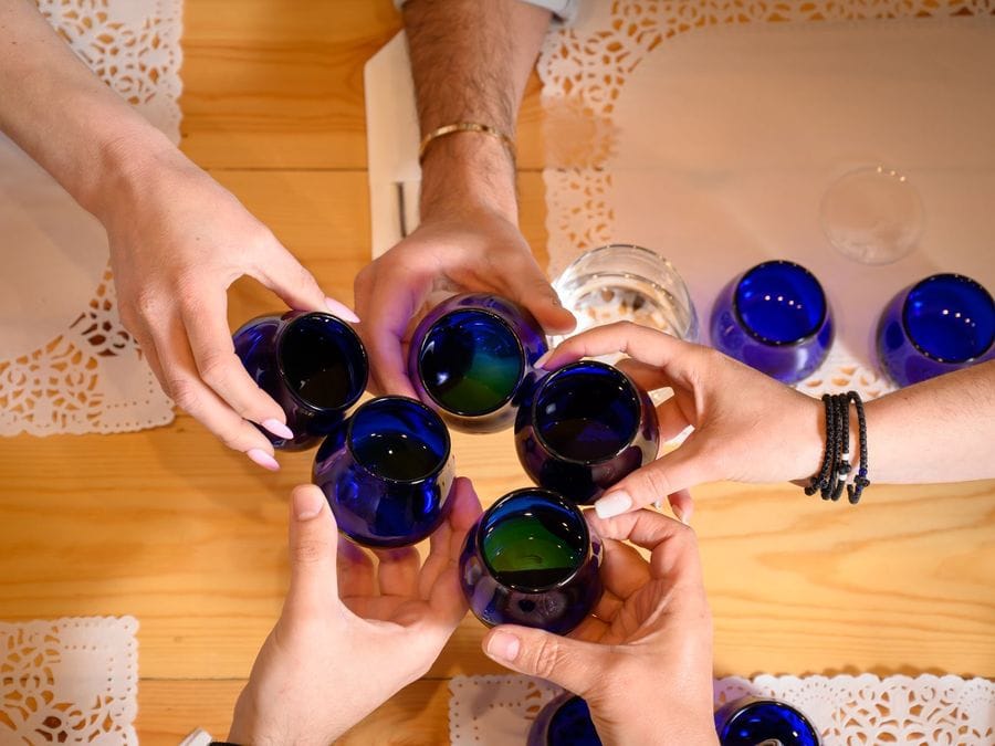 Five people joyfully clink their blue glasses filled with olive oil, celebrating the shared experience of savoring the liquid gold that delights their palates and brings them together.