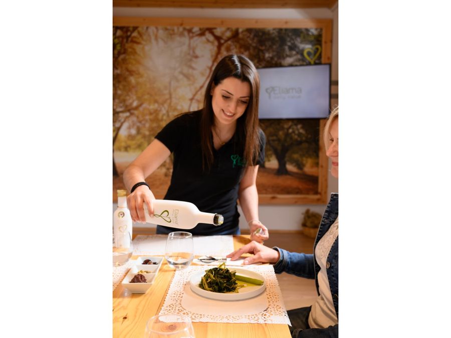 A woman gracefully pours olive oil onto a plate adorned with horta (leafy greens). The golden liquid cascades, enhancing the vibrant colors and tempting the taste buds.