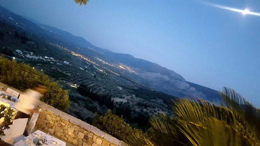 view from above from Lafkiotis Winery terrace with trees, illuminated buildings and mountains by night