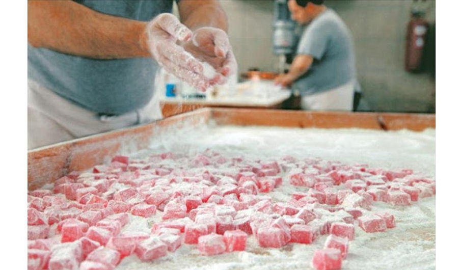 Close-up of woman sprinkling powder sugar with her hands on red Turkish delights on wooden frame