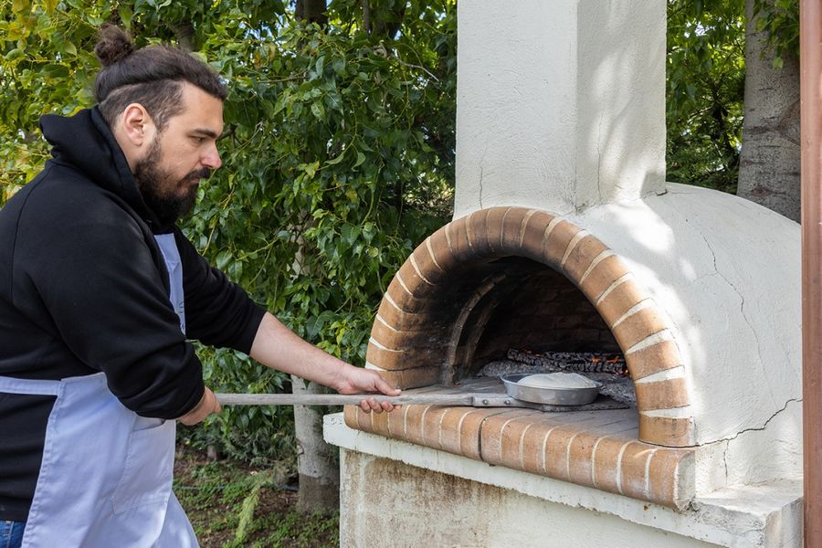 A man carefully places a baking pan filled with dough into a rustic wooden oven, as the heat embraces the creation, promising the delightful transformation of dough into a delectable baked masterpiece.