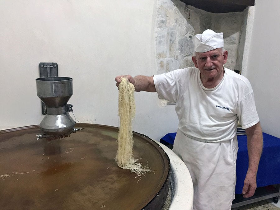 A skilled man meticulously prepares dough kataifi, his hands delicately separating and arranging fine strands, showcasing the artistry and precision of this traditional culinary technique.