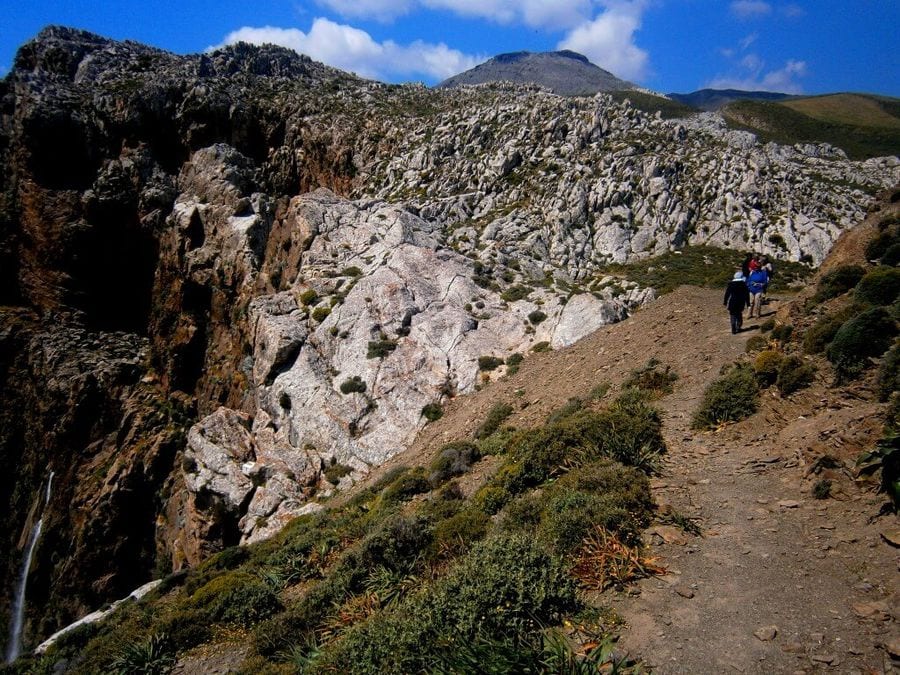 A group of people walks along a dusty road on a bluff. With determination in their strides, they explore the rugged terrain, united in their adventurous spirit.