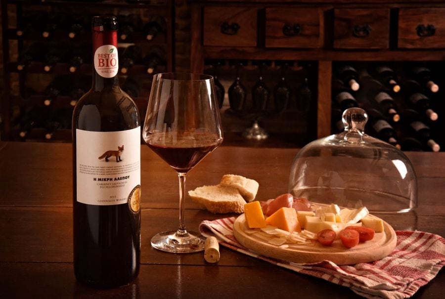 A table with a bottle of red wine and a plate with local cheeses and snacks