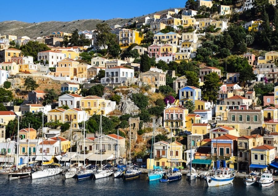 boats anchored in the port of Symi island in Greece and buildings on the mountain in the background