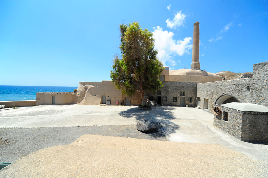 stony garden of 'Tomato Industrial Museum' with a tree in the middle, chimney and the sea in the background