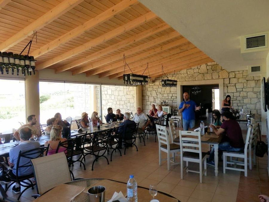 Tourists sitting at the tables in tasting room, enjoy a wine tasting and listening to a man giving a tour at Domaine Paterianakis
