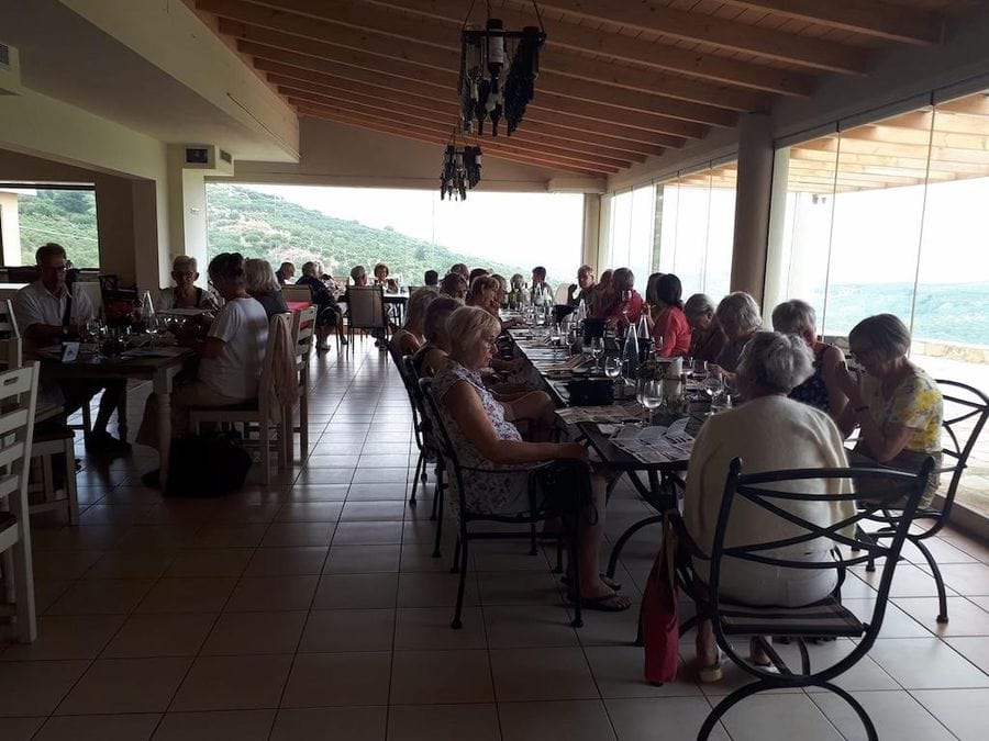 Tourists sitting at the tables in tasting room, enjoy a wine tasting and listening to a man giving a tour at Domaine Paterianakis