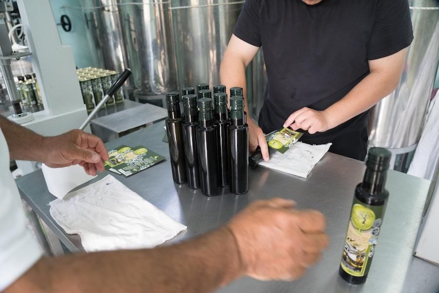 Two men putting labels on olive oil bottles at Yennima Yis plant